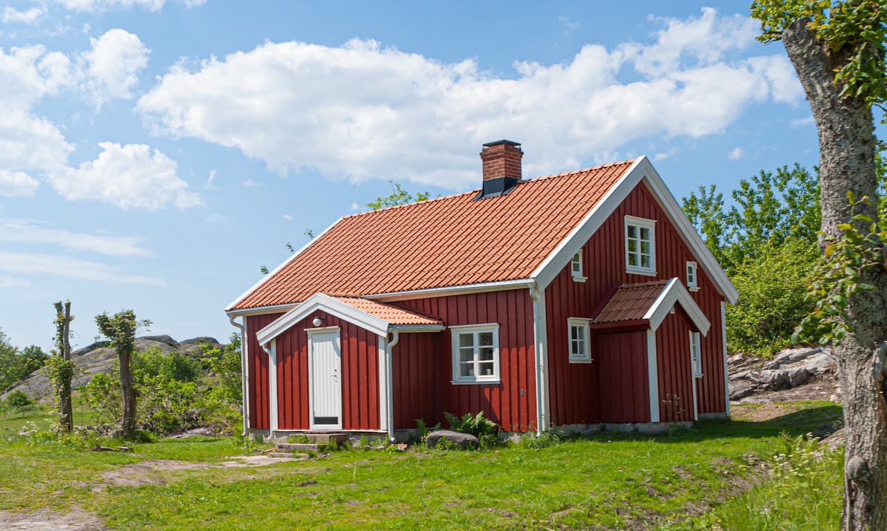 Picturesque red cottage under blue skies, surrounded by lush greenery in a rural setting.
